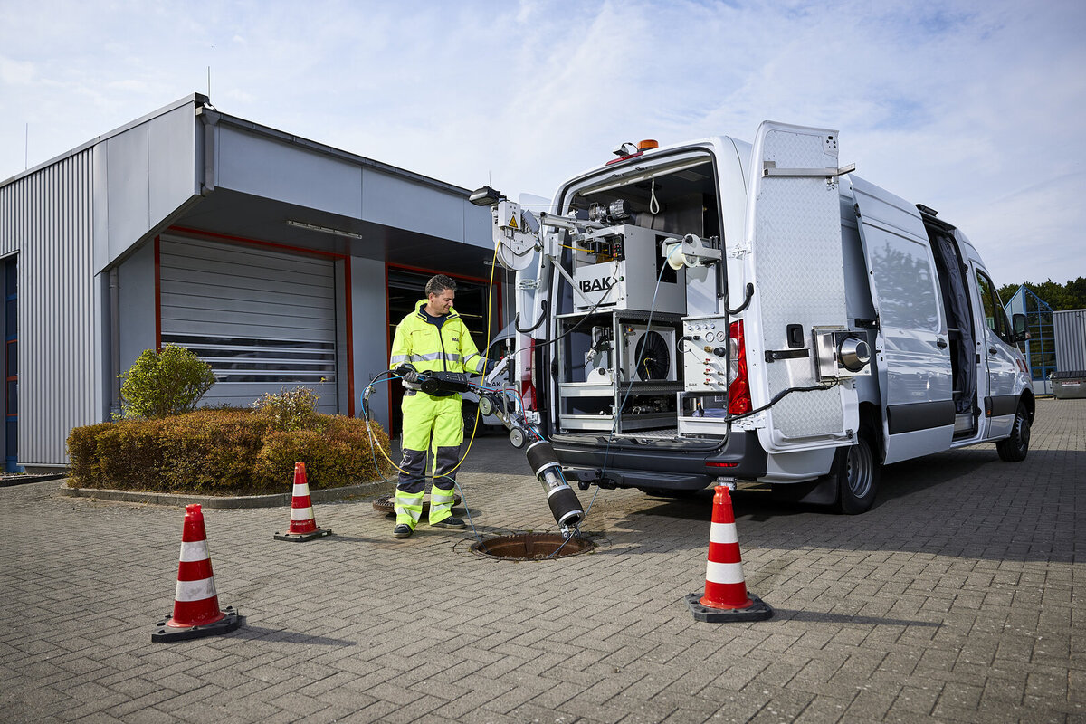 Bediener am Fahrzeugheck eines Dichtheitsprüfsystems beim Herablassen der Anlage in den Schacht